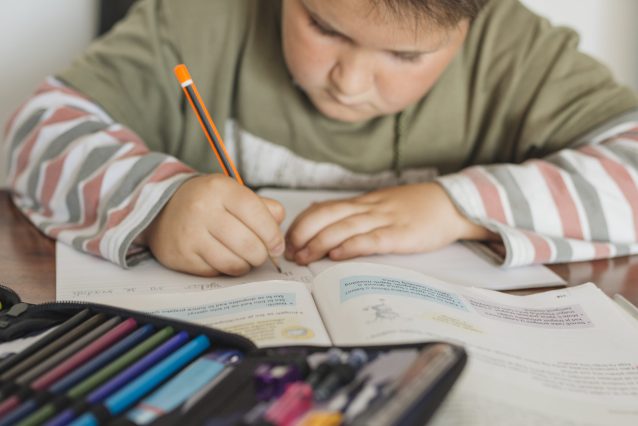 Criança concentrada escrevendo em caderno durante momento de estudo